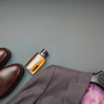 Article: Can you wear Chelsea Boots with a Suit? Image shows a suit oin ahnger with brown chelsea boots and a bottle of cologne