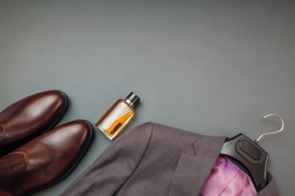 Article: Can you wear Chelsea Boots with a Suit? Image shows a suit oin ahnger with brown chelsea boots and a bottle of cologne