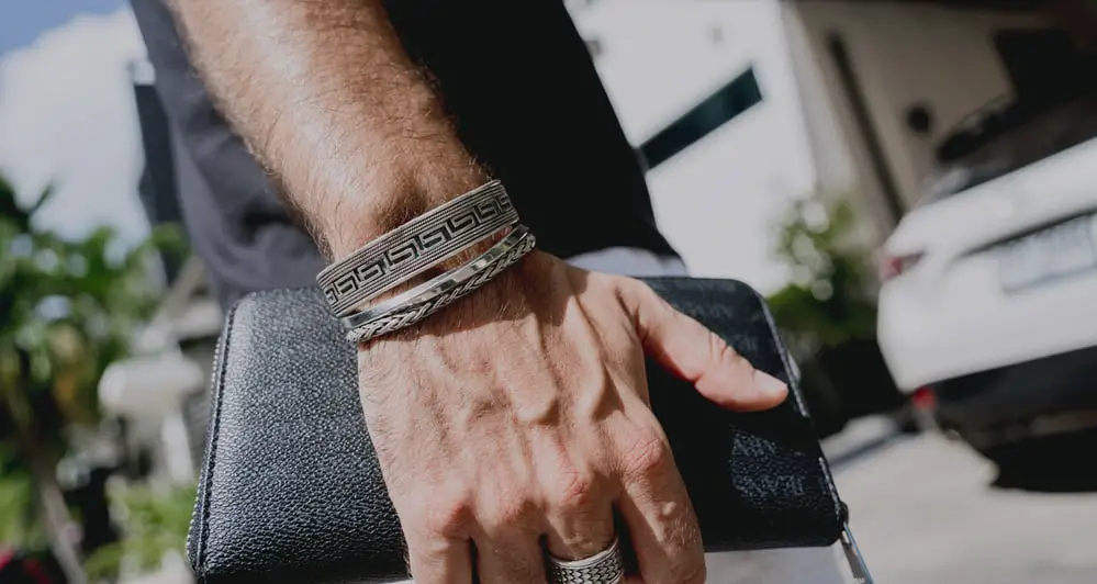 Man holding wallet in hand, three bracelets, one ring