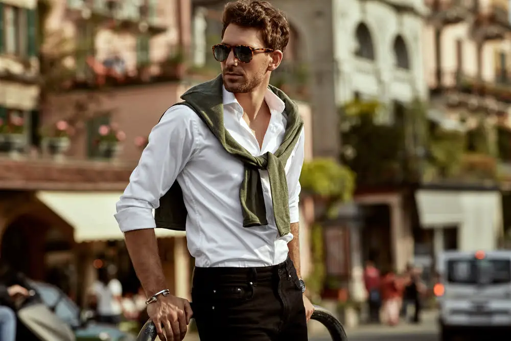 Stylish man wearing sunglasses and white shirt with tied sweater and bracelet