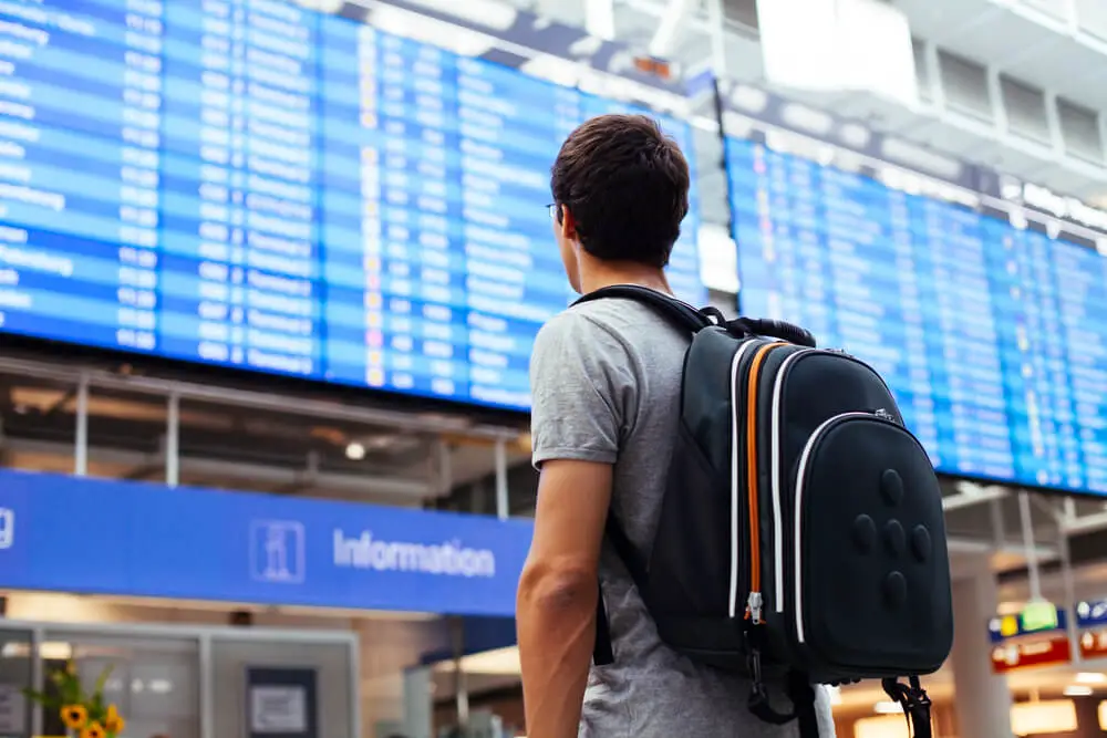 man with a travel backpack looking at flight departure board